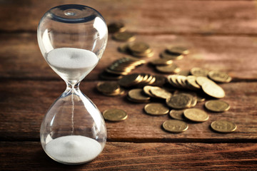 Hourglass and coins on wooden table close-up