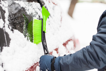 Transportation, winter, weather, people and vehicle concept - man cleaning snow from car with brush