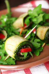 Zucchini rolls with cheese, bell peppers and arugula on plate, close-up, on table background