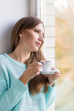 Young beautiful caucasian woman drinking her espresso at window sill
