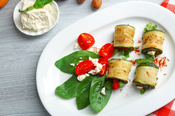 Zucchini rolls with cheese, bell peppers and arugula on plate, close-up, on table background