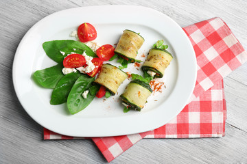 Zucchini rolls with cheese, bell peppers and arugula on plate, close-up, on table background
