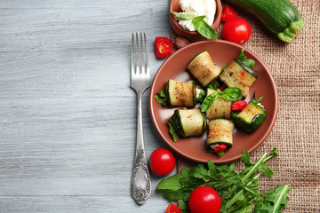 Salad with arugula and zucchini rolls on plate, on table background