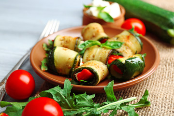 Salad with arugula and zucchini rolls on plate, on table background