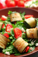 Salad with arugula and zucchini rolls on plate, on table background
