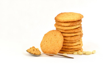 Neat stack of homemade peanut butter cookies with one resting against it, scattered peanurs and peanut butter on a spoon. On a white background.