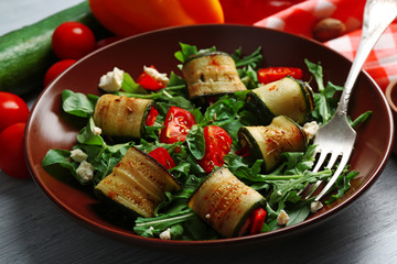 Salad with arugula and zucchini rolls on plate, on table background
