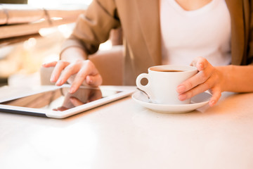 young woman holding cup of coffee in cafe with tablet