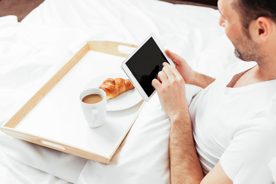 Surfing in the bed! Man sitting in bed and holding a tablet