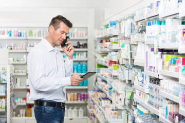 Customer Using Mobile Phone And Digital Tablet In Pharmacy