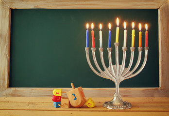 low key image of jewish holiday Hanukkah with menorah (traditional Candelabra) and wooden dreidels spinning top with chalkboard background, room for text
