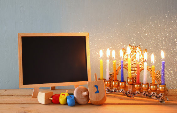 low key image of jewish holiday Hanukkah with menorah (traditional Candelabra) and wooden dreidels spinning top with chalkboard background, room for text
