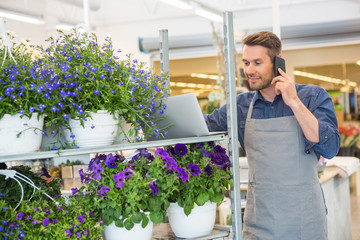 Florist Using Mobile Phone And Laptop In Shop