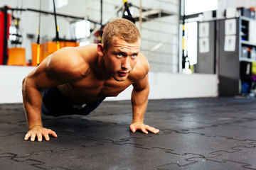Young muscular athlete doing suspension pushups - obrazy, fototapety, plakaty