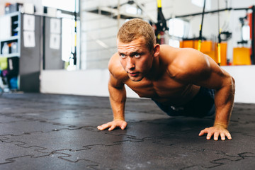 Young muscular athlete practicing suspension pushups - obrazy, fototapety, plakaty