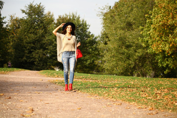 Young woman in fashion blue jeans and red bag walking in autumn