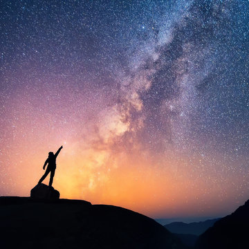 Catch the star. A person is standing next to the Milky Way galaxy pointing on a bright star.