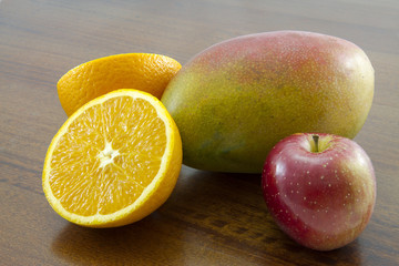 Combination of fruit over a wooden table: sliced orange, mango and apple