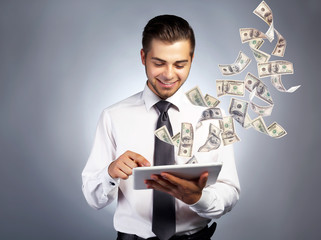 Businessman holding tablet with money fly out of it
