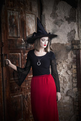 Beautiful witch standing in front of the door of haunted house