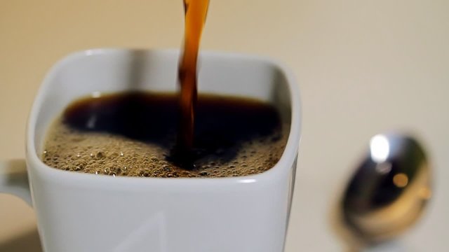 Coffee Pour Tilt Close Up. a close up tilting shot of coffee being poured into a white coffee mug. Shallow depth of field. silver spoon blurred in background
