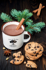Spicy hot chocolate with cinnamon stick and chocolate chip cookies over dark wooden background.