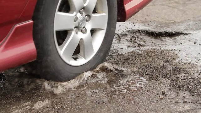 Car Hits Two Pot Holes. slow motion of a car driving through two potholes filled with water. splashing everywhere. 
