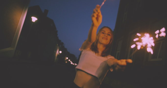 Grunge teen girl holding sparklers on city street at night