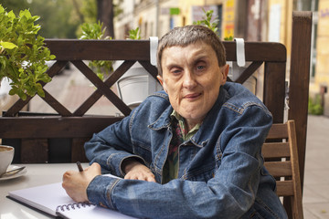 Adult disabled man with cerebral palsy sitting with a notebook at an outdoor cafe.