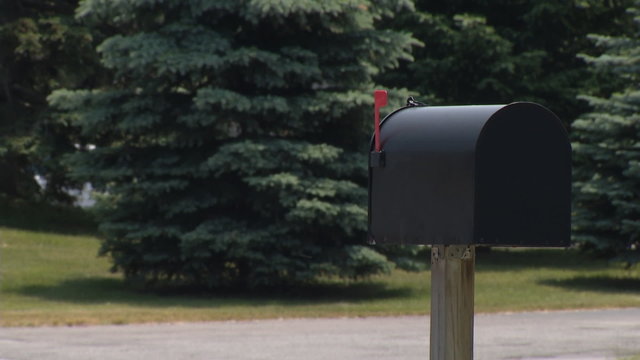 Mailbox with Heavy Traffic. Focus on a black mailbox with red flag up. Traffic is very heavy in the background. cars and trucks fly by. Trees in Background
