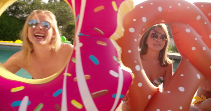 Smiling girl friends with funny pool inflatables outdoors 