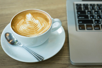 Hot art Latte Coffee in a cup on wooden table and and laptop in