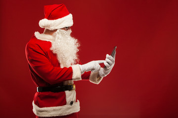 Modern Santa Claus using tablet pc over red background