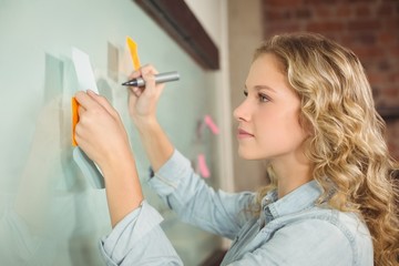Woman holding sticky note while writing on glass board