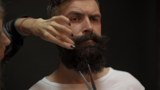 Girl with scissors cuts and an electric beard and mustache handsome bearded man in the studio on a black background