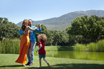 Obraz premium Happy parents are dancing on grass at park on a weekend day all together