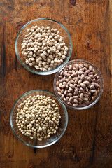 Bowls of various legumes (soybeans, chickpeas, beans) on wooden