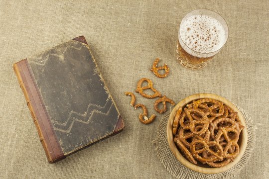 Beer in a glass and a book on the table.
Crispy wheat straw with salt. Pile of pretzel sticks. Entertainment to watch TV.

