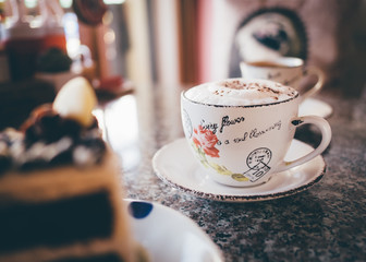 Cappuccino coffee cup on a table. Vintage retro style photo with color filters, vignette effect, and some fine film noise added.