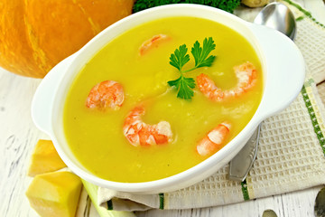 Soup-puree pumpkin with shrimp in white bowl on board