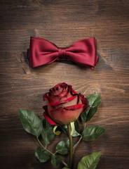 A red rose and a bow tie lying on the wooden table