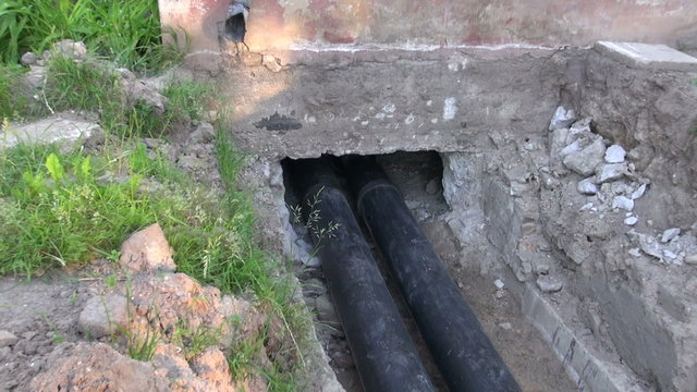 Two black water heating pipes in a ditch going inside the house 