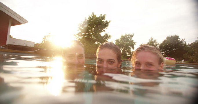 Portrait of three girls submerged in swimming pool at sunset