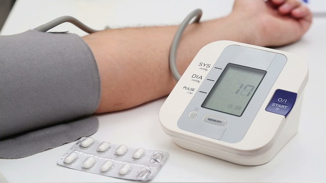 Man measuring his blood pressure at home, the instrument is pumping up.