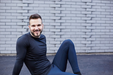 Sport man with beard stretching against concrete wall