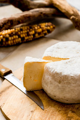 whole caciotta cheese with slice over chopping board and knife