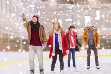 Obraz premium happy friends pointing finger on skating rink