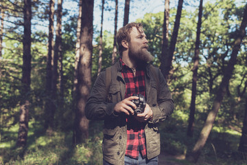 Observing beard man holding vintage camera in forest.