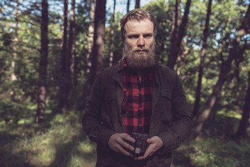 Naklejka na ściany i meble Observing beard man holding vintage camera in forest.