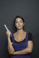 Fototapeta premium Bella ragazza con espressione determinata indossa tuta da meccanico e tiene in mano chiave inglese